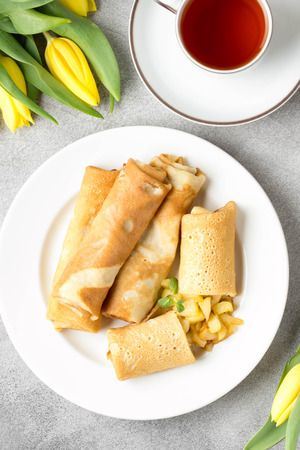 Thin pancakes (crepes) with apple filling, stuffed rolls, Russian traditional food for maslenitsa, French dessert, breakfast with tulips on mother's dayの写真素材