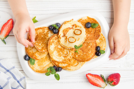 Hands of a small child to reach for pancakes with a smile. Maslennitsa, pancakes with berries on a white backgroundの写真素材
