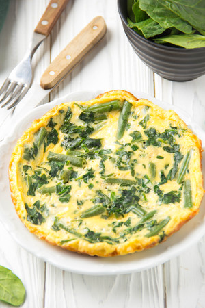 Omelet with spinach and green beans, healthy food. Egg and milk Frittata, delicious Breakfast on white wooden backgroundの写真素材