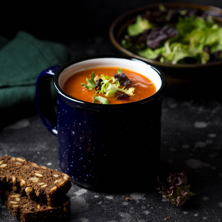 Red vegetable cream soup in blue mug (tomato, carrot, lentil, pumpkin), delicious hot homemade lunch in cup. Dark backgroundの写真素材