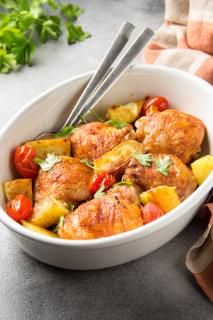 Baked chicken thighs (legs) with crispy crust, potatoes and cherry tomatoes. Simple delicious homemade dinner, traditional meal. Everyday food cooked in ovenの写真素材
