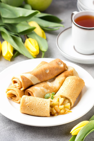Thin pancakes (crepes) with apple filling, stuffed rolls, Russian traditional food for maslenitsa, French dessert, breakfast with tulips on mother's dayの写真素材