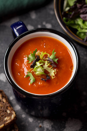 Red vegetable cream soup in blue mug (tomato, carrot, lentil, pumpkin), delicious hot homemade lunch in cup. Dark backgroundの写真素材