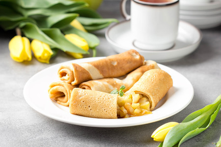 Thin pancakes (crepes) with apple filling, stuffed rolls, Russian traditional food for maslenitsa, French dessert, breakfast with tulips on mother's dayの写真素材