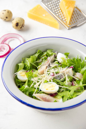 Fresh salad with salted herring, fish, lettuce, boiled quail eggs, red onions and hard Parmesan cheese. Delicious lunch, spring green foodの写真素材