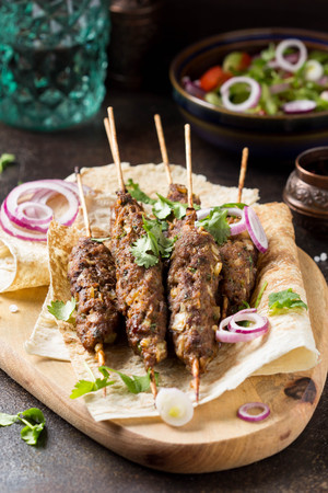 Lula kebab from minced meat (beef, lamb, veal) on pita bread (lavash), shish kebab. With red onion, cilantro and vegetable saladの写真素材
