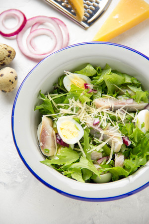 Fresh salad with salted herring, fish, lettuce, boiled quail eggs, red onions and hard Parmesan cheese. Delicious lunch, spring green foodの写真素材