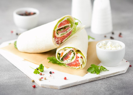Tortilla with salmon, lettuce and cream cheese. Delicious snack wraps with fish and salad. Healthy burrito with pita bread for breakfastの写真素材