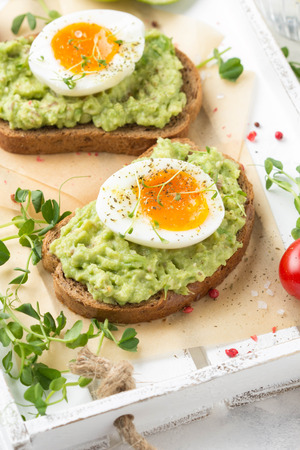 Toast with avocado puree and soft boiled egg on white tray, liquid yolk, delicious breakfast, light sandwich. Healthy foodの写真素材