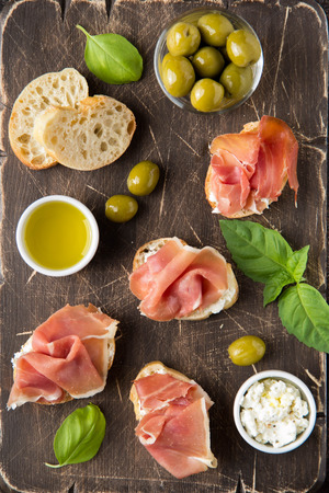 Toast with serrano ham (jamon, prosciutto crudo, hamon), traditional Italian antipasti. Delicious snack with bread, cream cheese, olives. Health food, appetizer for wine, bruschettaの写真素材
