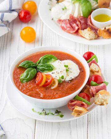 Tomato cold gazpacho soup with fresh vegetables, mozzarella, salami, croutons and basil. Traditional Spanish summer foodの写真素材
