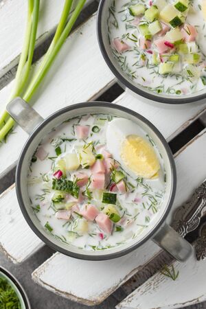 Traditional cold Russian soup okroshka, with sausage (ham), potatoes, boiled egg, fresh vegetables (cucumber, radish), green onions and dill. Yogurt, kefir, mineral water. Summer foodの写真素材