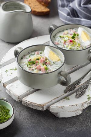 Traditional cold Russian soup okroshka, with sausage (ham), potatoes, boiled egg, fresh vegetables (cucumber, radish), green onions and dill. Yogurt, kefir, mineral water. Summer foodの写真素材