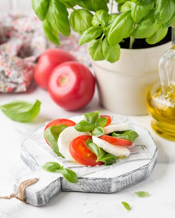 Caprese salad with mozzarella, juicy tomato and fresh Basil. A delicious Italian snack, traditional food. On light backgroundの写真素材