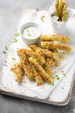 Zucchini sticks in breadcrumbs, with cheese, herbs, breadcrumbs and white yogurt sauce. Healthy tasty snack, summer foodの写真素材
