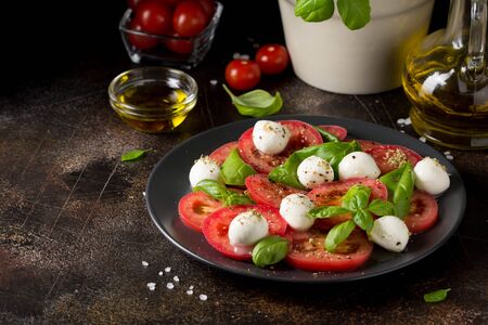 Caprese salad with mini mozzarella, juicy tomato and fresh Basil. A delicious Italian snack, traditional food. On dark backgroundの写真素材