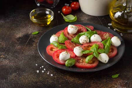 Caprese salad with mini mozzarella, juicy tomato and fresh Basil. A delicious Italian snack, traditional food. On dark backgroundの写真素材