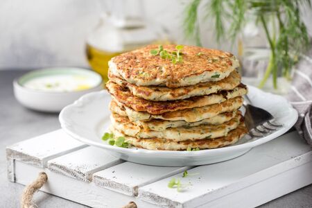 Chicken pancakes with zucchini and herbs, stack of cutlets on plate. Delicious summer food, healthy lunch with meat, vegetables and yogurt sauceの写真素材