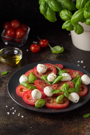 Caprese salad with mini mozzarella, juicy tomato and fresh Basil. A delicious Italian snack, traditional food. On dark backgroundの写真素材