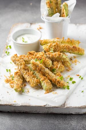 Zucchini sticks in breadcrumbs, with cheese, herbs, breadcrumbs and white yogurt sauce. Healthy tasty snack, summer foodの写真素材