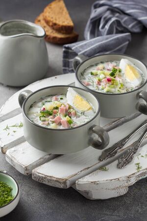 Traditional cold Russian soup okroshka, with sausage (ham), potatoes, boiled egg, fresh vegetables (cucumber, radish), green onions and dill. Yogurt, kefir, mineral water. Summer foodの写真素材