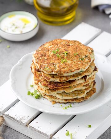 Chicken pancakes with zucchini and herbs, stack of cutlets on plate. Delicious summer food, healthy lunch with meat, vegetables and yogurt sauceの写真素材