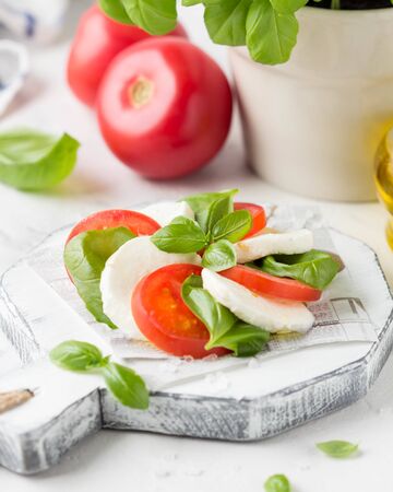 Caprese salad with mozzarella, juicy tomato and fresh Basil. A delicious Italian snack, traditional food. On light backgroundの写真素材