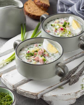 Traditional cold Russian soup okroshka, with sausage (ham), potatoes, boiled egg, fresh vegetables (cucumber, radish), green onions and dill. Yogurt, kefir, mineral water. Summer foodの写真素材