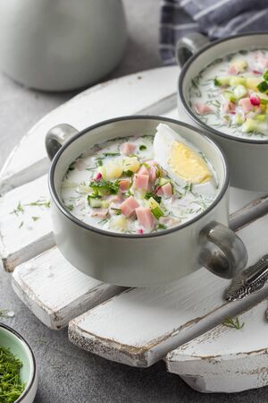 Traditional cold Russian soup okroshka, with sausage (ham), potatoes, boiled egg, fresh vegetables (cucumber, radish), green onions and dill. Yogurt, kefir, mineral water. Summer foodの写真素材