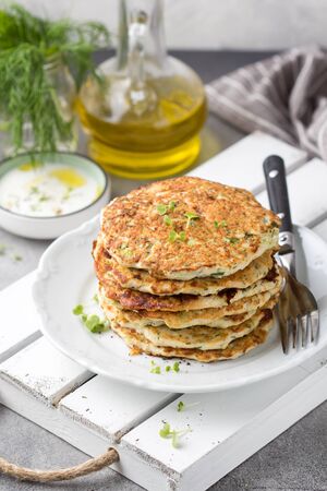Chicken pancakes with zucchini and herbs, stack of cutlets on plate. Delicious summer food, healthy lunch with meat, vegetables and yogurt sauceの写真素材