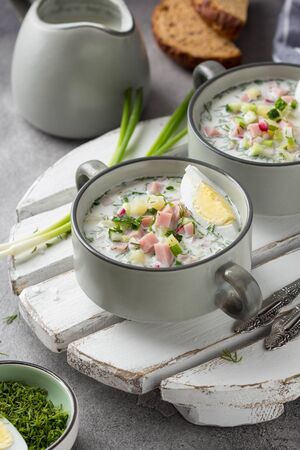Traditional cold Russian soup okroshka, with sausage (ham), potatoes, boiled egg, fresh vegetables (cucumber, radish), green onions and dill. Yogurt, kefir, mineral water. Summer foodの写真素材