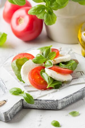 Caprese salad with mozzarella, juicy tomato and fresh Basil. A delicious Italian snack, traditional food. On light backgroundの写真素材