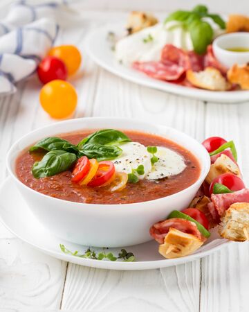 Tomato cold gazpacho soup with fresh vegetables, mozzarella, salami, croutons and basil. Traditional Spanish summer foodの写真素材