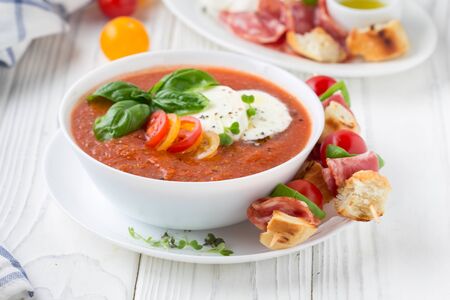 Tomato cold gazpacho soup with fresh vegetables, mozzarella, salami, croutons and basil. Traditional Spanish summer foodの写真素材