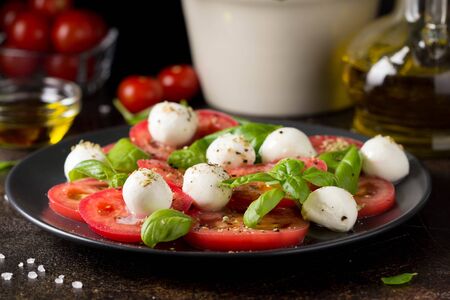 Caprese salad with mini mozzarella, juicy tomato and fresh Basil. A delicious Italian snack, traditional food. On dark backgroundの写真素材