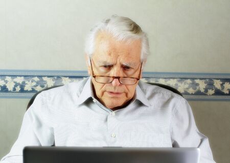 Senior gentleman with glasses in front of computer with concentrated and worried expressionの写真素材