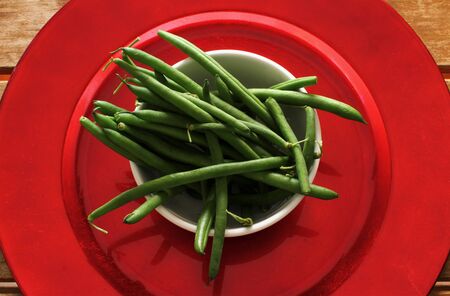 Overhead photo of a white bowl with raw green beans on a wooden slatted table.
