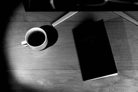 Closed book, cup with coffee and computer monitor. Top view, black and white photo.の写真素材