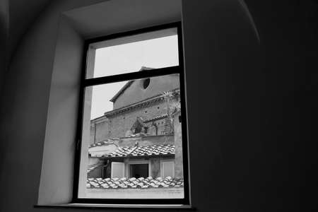 Window on a glimpse of Rome. Small church, roofs and tiles. Black and white photo.