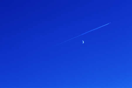 Airplane wake and quarter moon in the blue sky.の写真素材