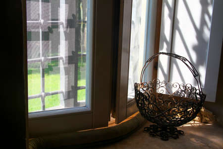 Wrought iron basket on a window sill inside a country house. Reflections of light and shadows.の写真素材
