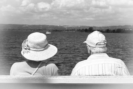Elderly couple sitting on a bench by the lake. Black and white photo.の写真素材