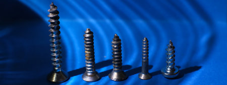 Macro photo, row of five steel screws, shadows and blue background.