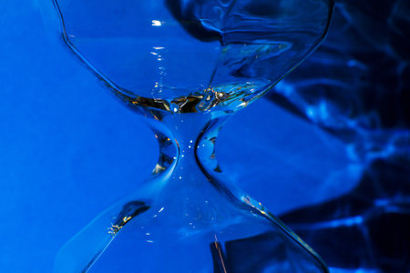 Macro photo, glass hourglass detail, shadows and bright blue background.の写真素材