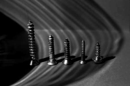 Macro photography, row of five steel screws, shadows, black and white photo.