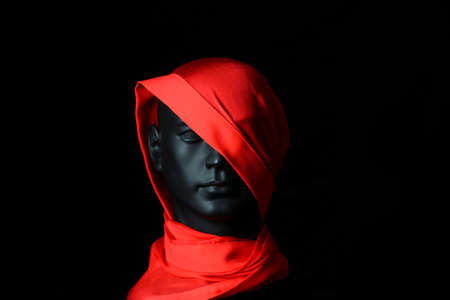 Black plastic mannequin head with large red silk scarf covering half face, black background.の写真素材