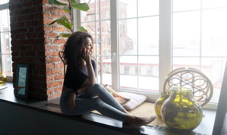 Brazilian happy woman with African curls speaking on cellphone at home or cafe indoors. Communication with friends of relatives. Comfort relationships. Freelanceの写真素材
