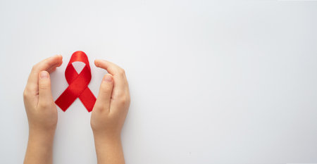 AIDs red ribbon in child hands on white background, symbol of struggle against HIV, AIDS and cancer....