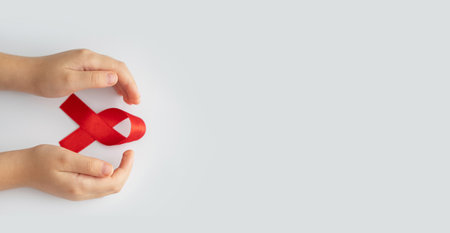 AIDs red ribbon in child hands on white background, symbol of struggle against HIV, AIDS and cancer....