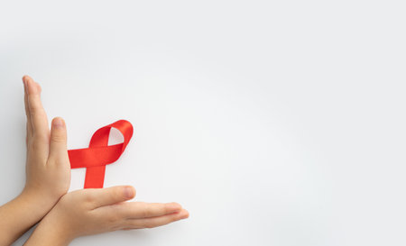 AIDs red ribbon in child hands on white background, symbol of struggle against HIV, AIDS and cancer....